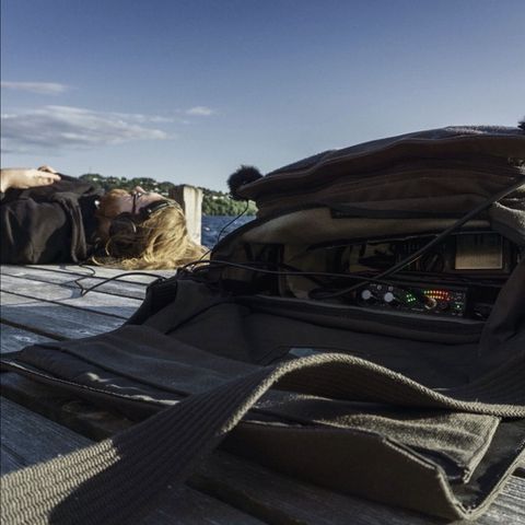 Man laying down wearing headphones plugged into audio recorder
